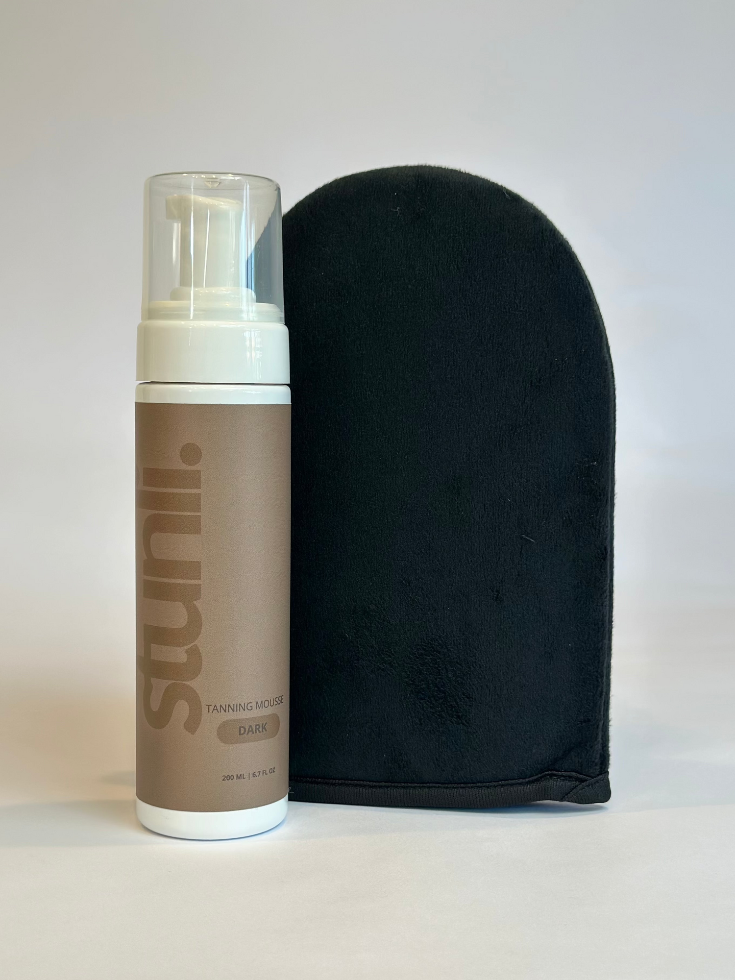 A bottle of Stunli self-tanning lotion next to a black application mitt.