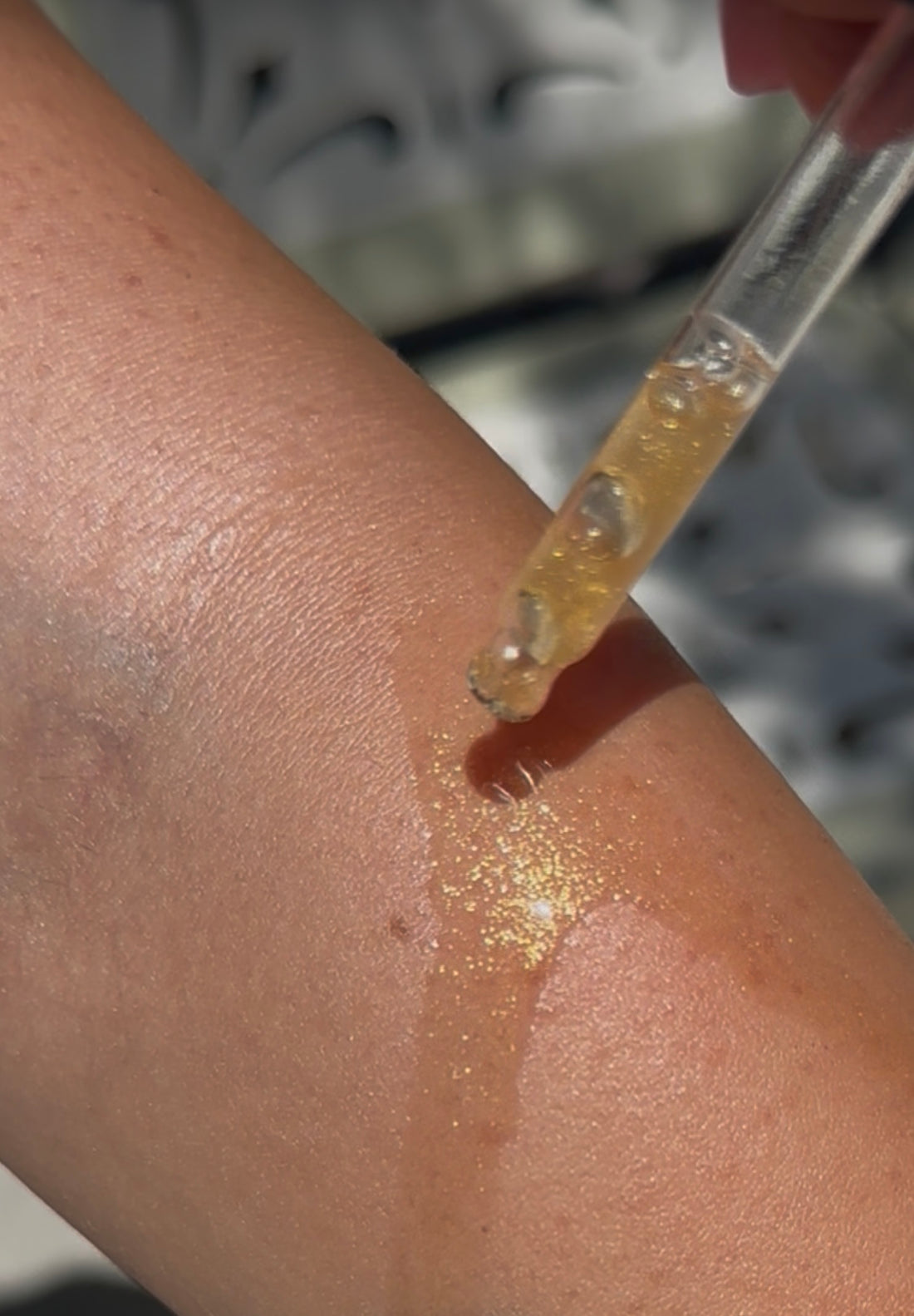 Close-up of a hand applying a golden shimmering substance to skin with a dropper.