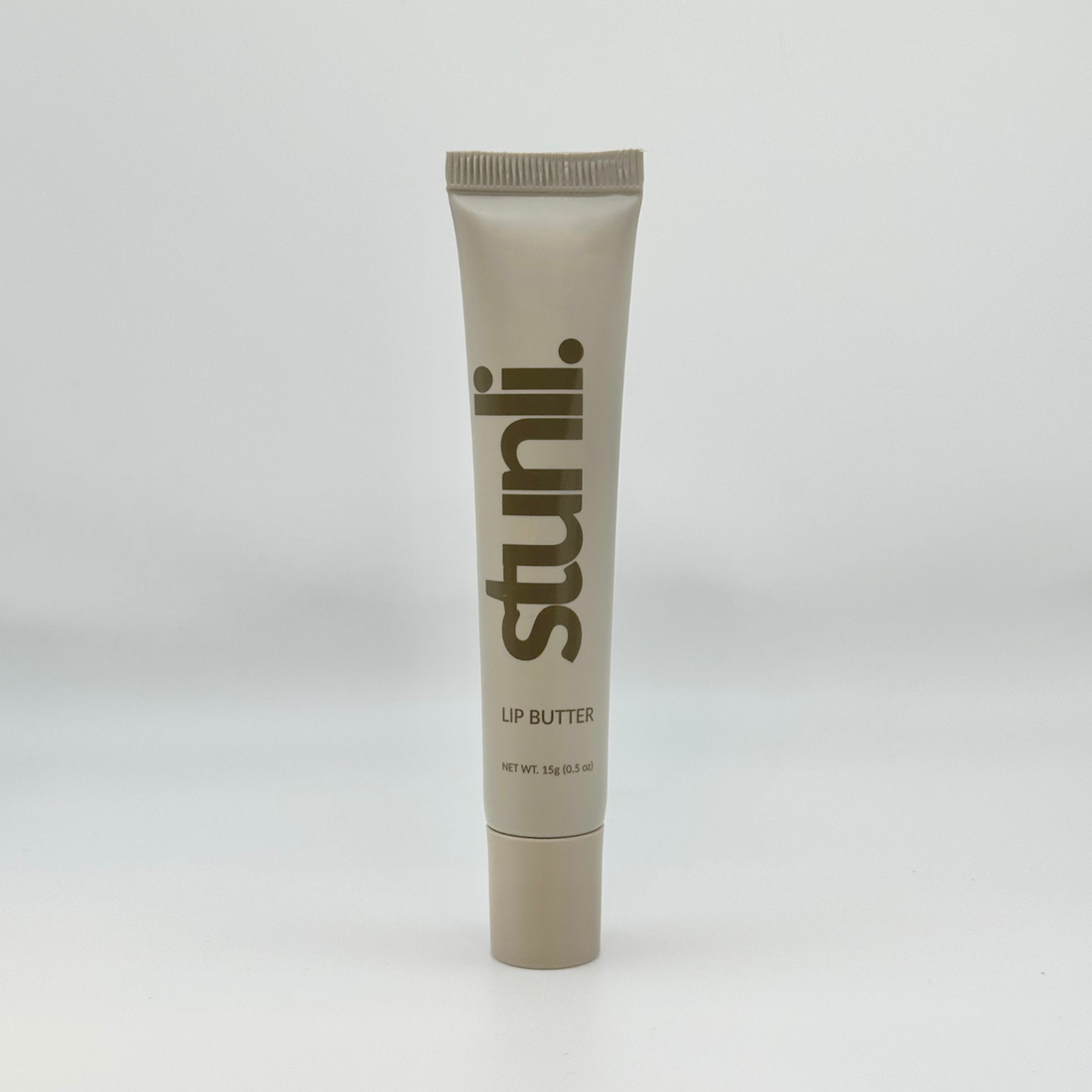 A single tube of Stunli lip butter in a warm taupe-beige color, standing upright against a light gray studio background.