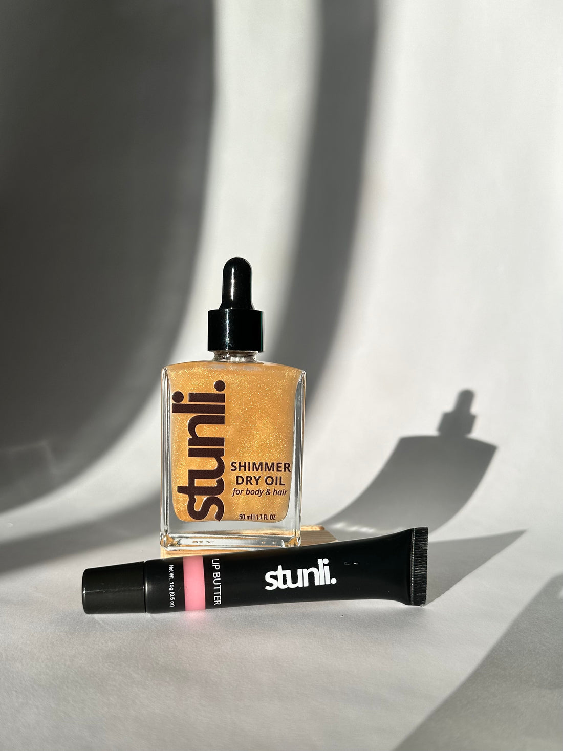A gift set of Stunli Shimmer Oil and Stunli Lip Butter tube on a gray baackground