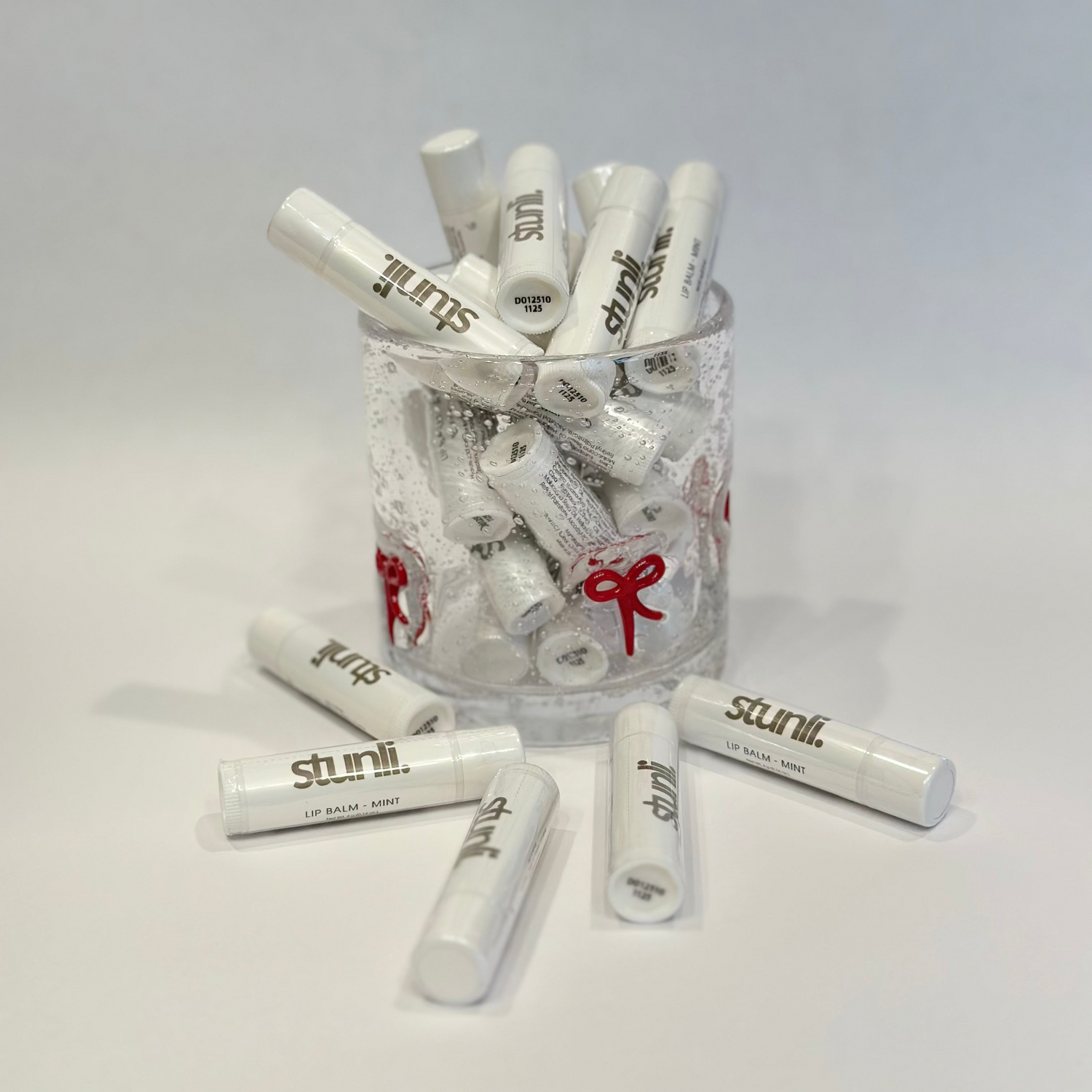 Clear glass jar filled with white lip balm tubes on a light gray background