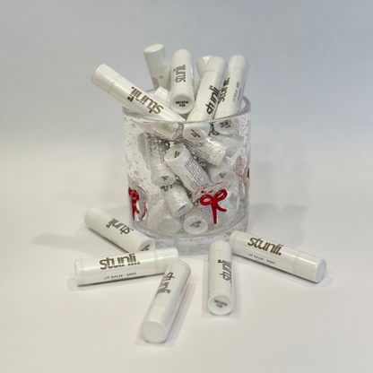 Clear glass jar filled with white lip balm tubes on a light gray background